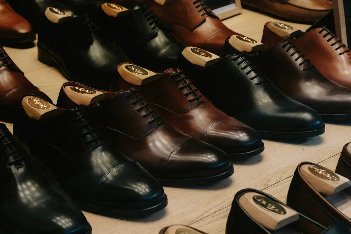 Rows of polished brown and black leather dress shoes with wooden shoe trees inside, neatly arranged on a light wood surface.