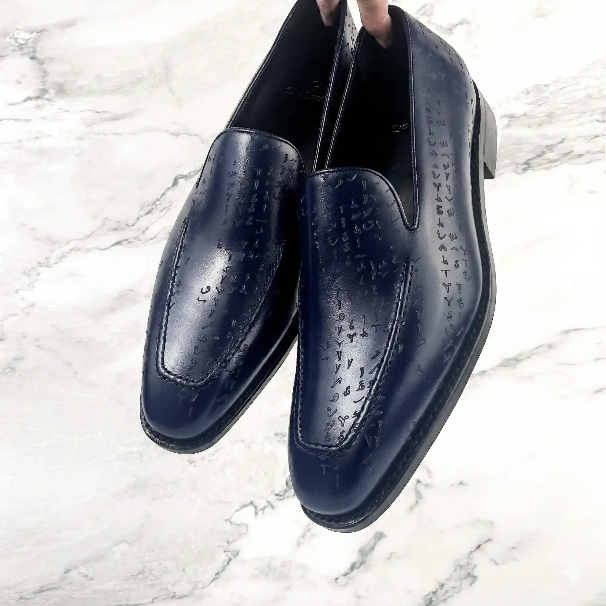 Deep navy leather loafers with a subtle embossed script pattern across the upper.
