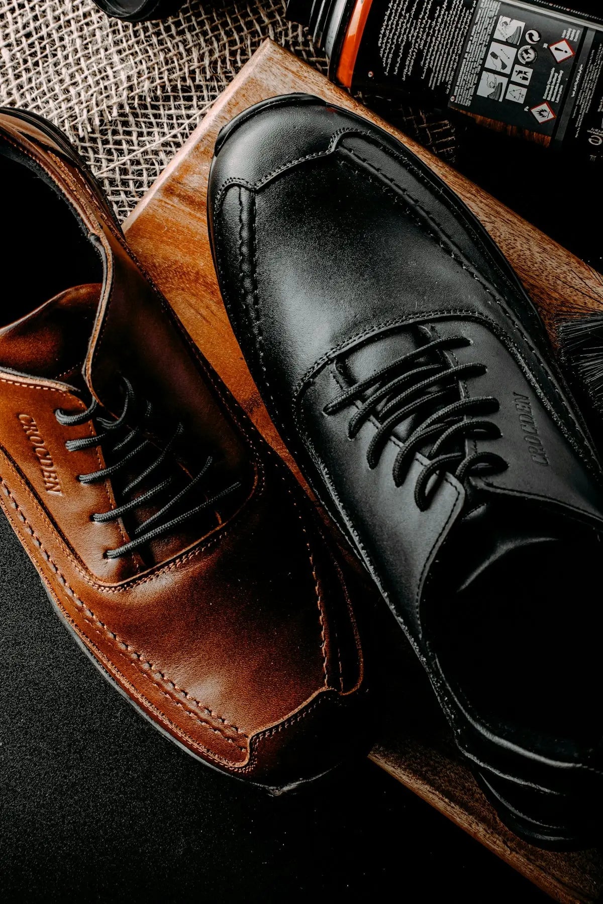 A pair of polished black leather dress shoes with contrasting stitching and matching laces, alongside a brown leather shoe.