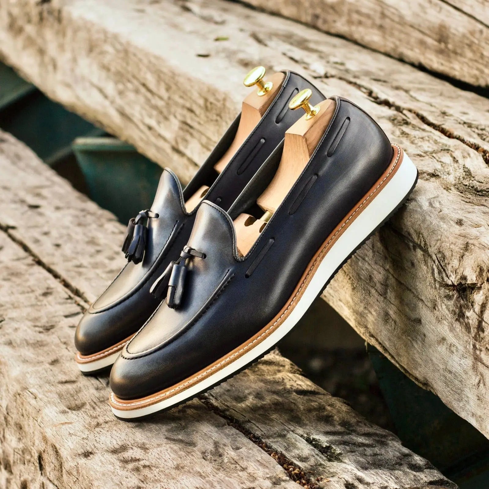 Black leather tassel loafers with tan stitching and a white rubber sole.