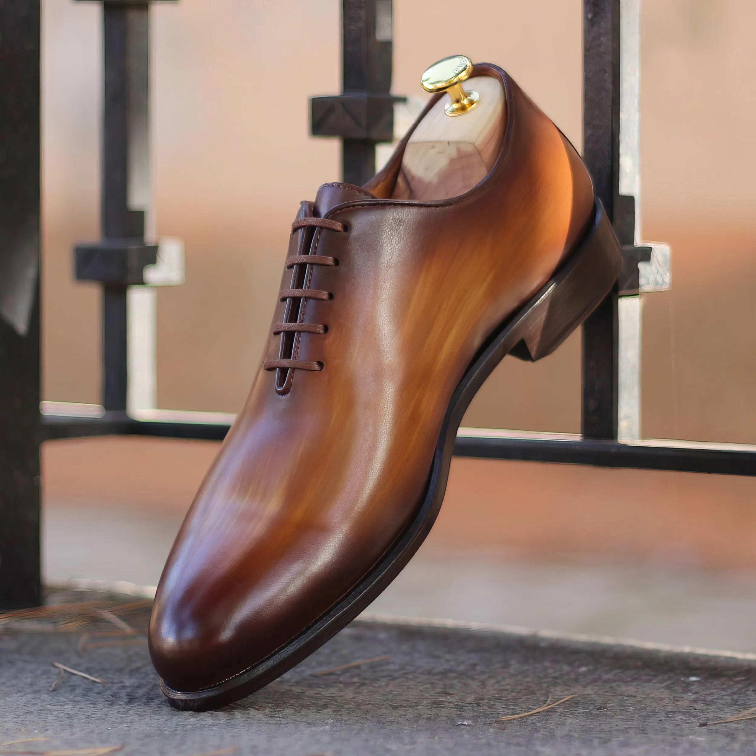 A polished brown leather oxford shoe with a subtle gradient finish and dark laces.