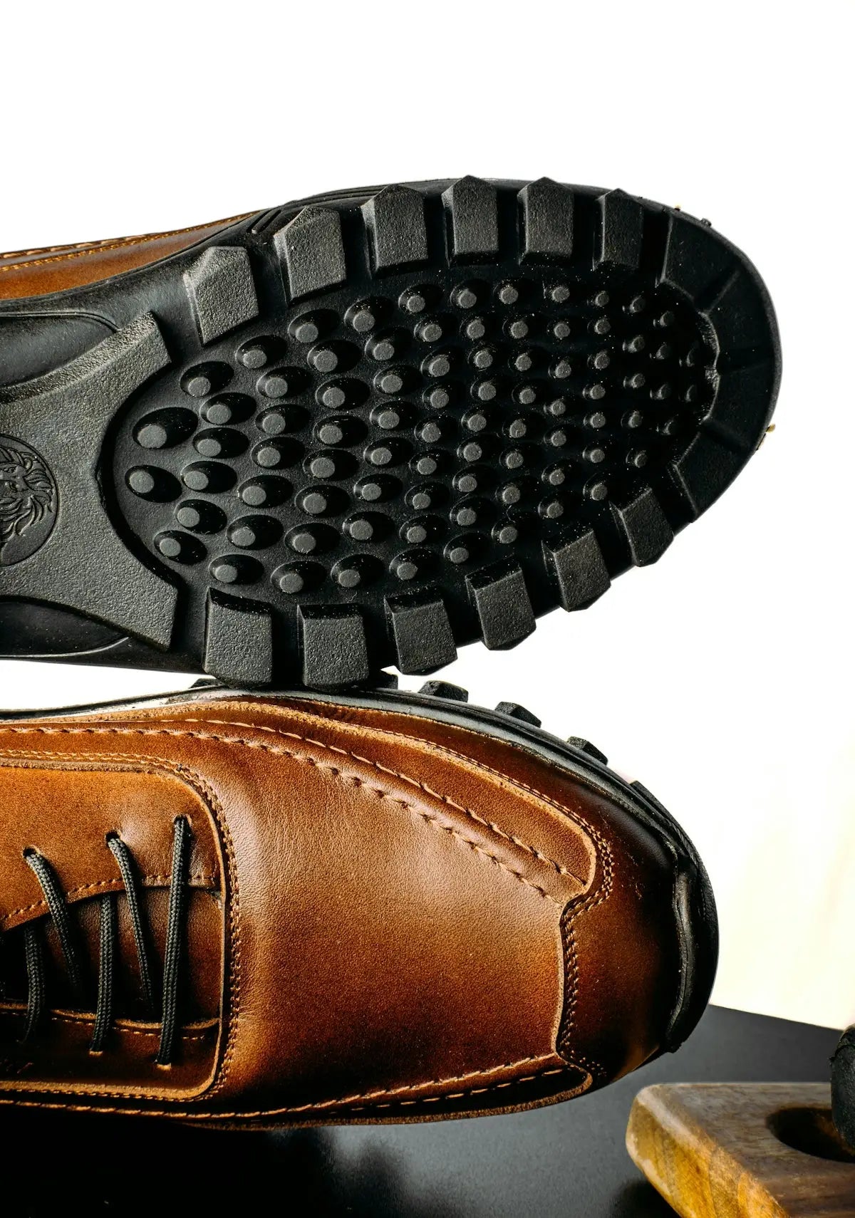 Brown leather lace-up men’s dress shoe with black laces and a rugged, textured rubber sole.
