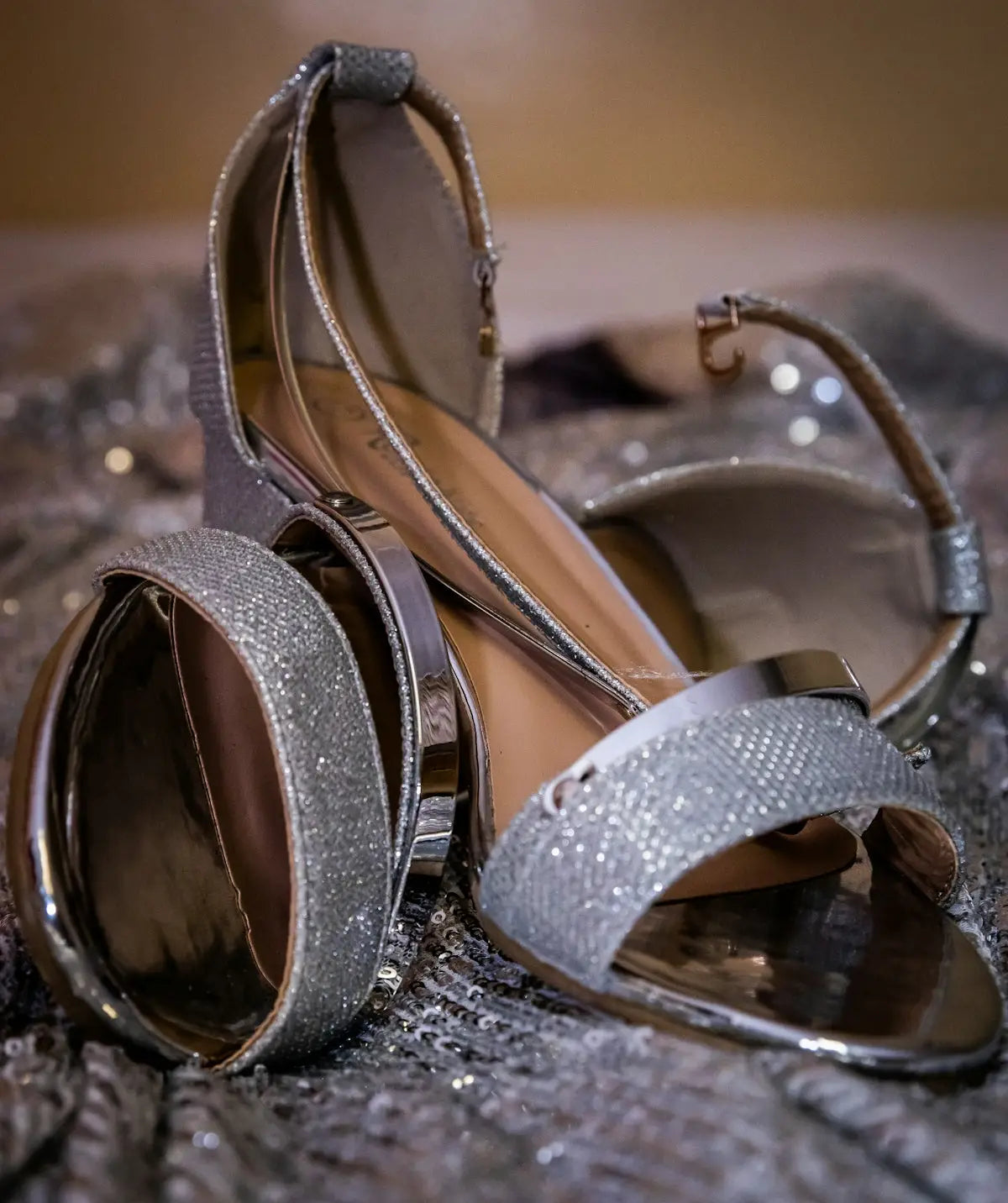 Shiny silver glittery high-heeled sandals with metallic straps and a sleek, modern design.