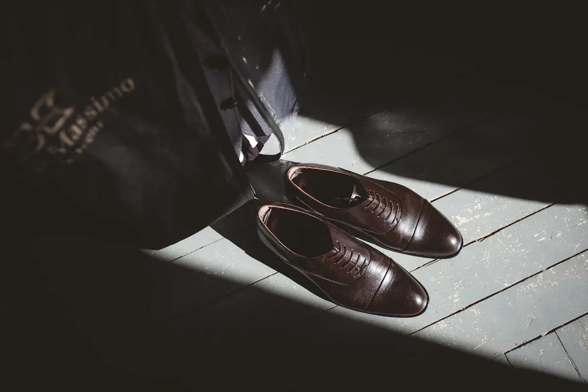 A pair of dark brown leather oxford shoes with a classic cap-toe design, resting on a wooden floor.